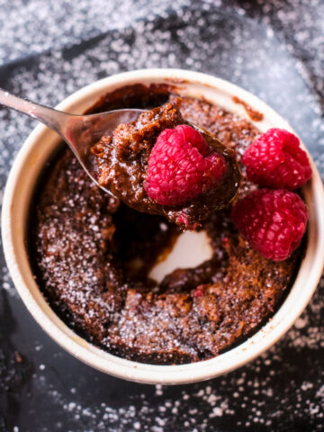 chocolate self saucing pudding in a ramekin with raspberries, showing spoonful of pudding & chocolate sauce