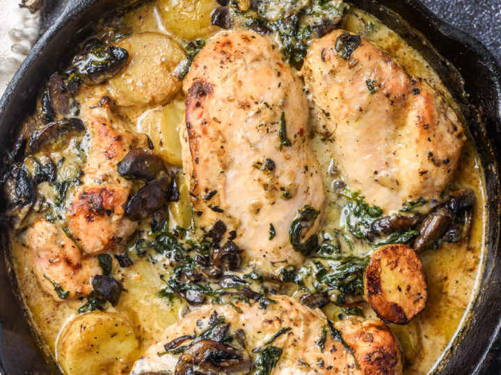 4 chicken breasts, mushrooms, baby potatoes and spinach all cooked in a cast iron pan on a dark background