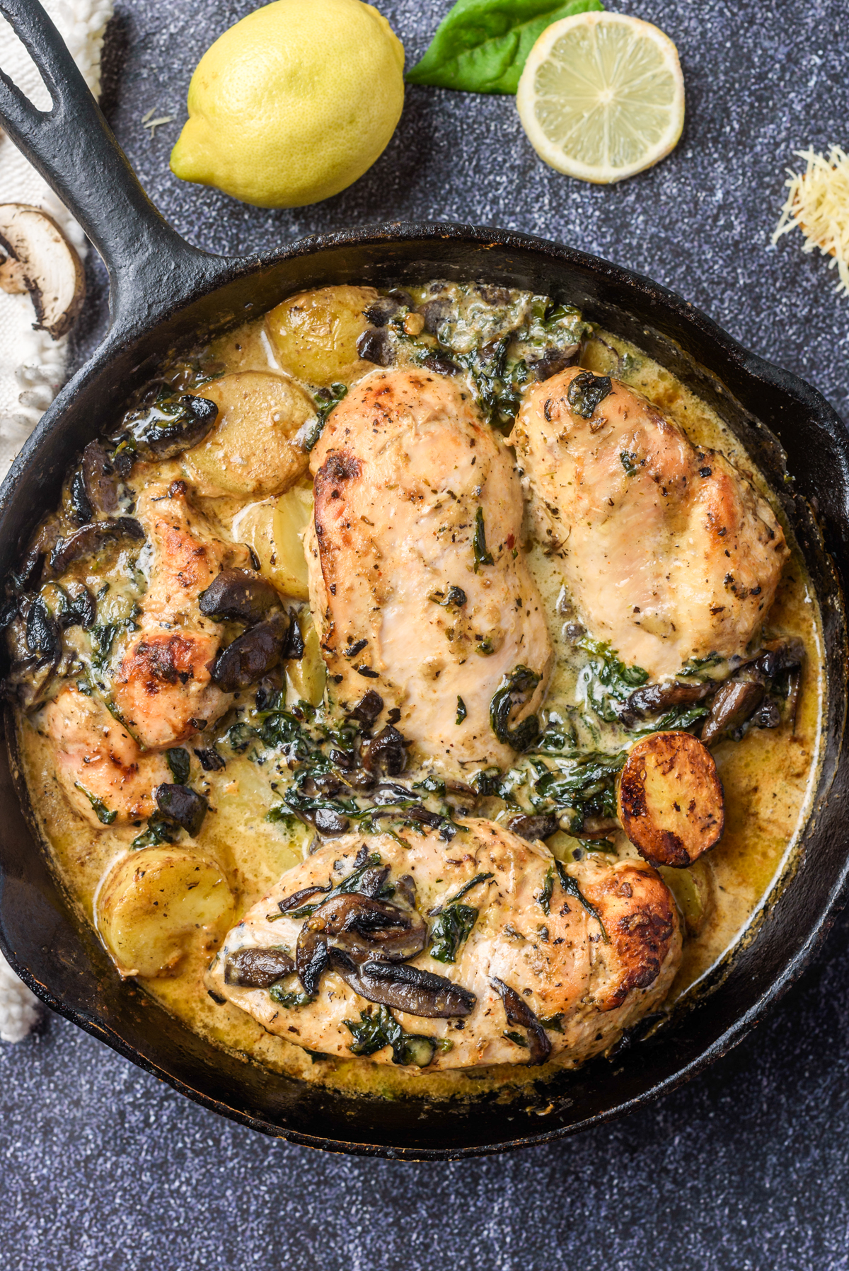4 chicken breasts, mushrooms, baby potatoes and spinach all cooked in a cast iron pan on a dark background 