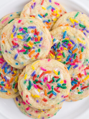 funfetti sugar cookies piled on a white plate, white background.