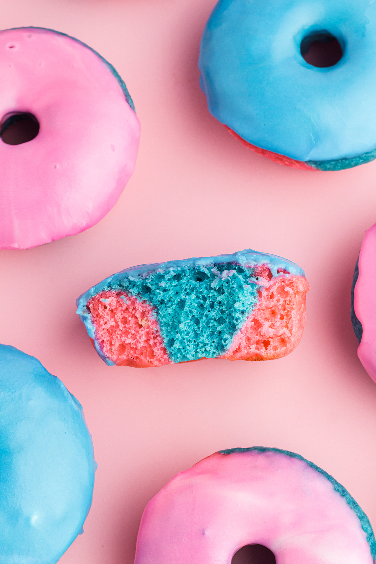 half donut in the middle to see inside, surrouned by 5 other donuts but you can only see parts of the other donuts, pink top left, blue top right, pink middle right, pink bottom right a bit towards the middle, blue bottom left