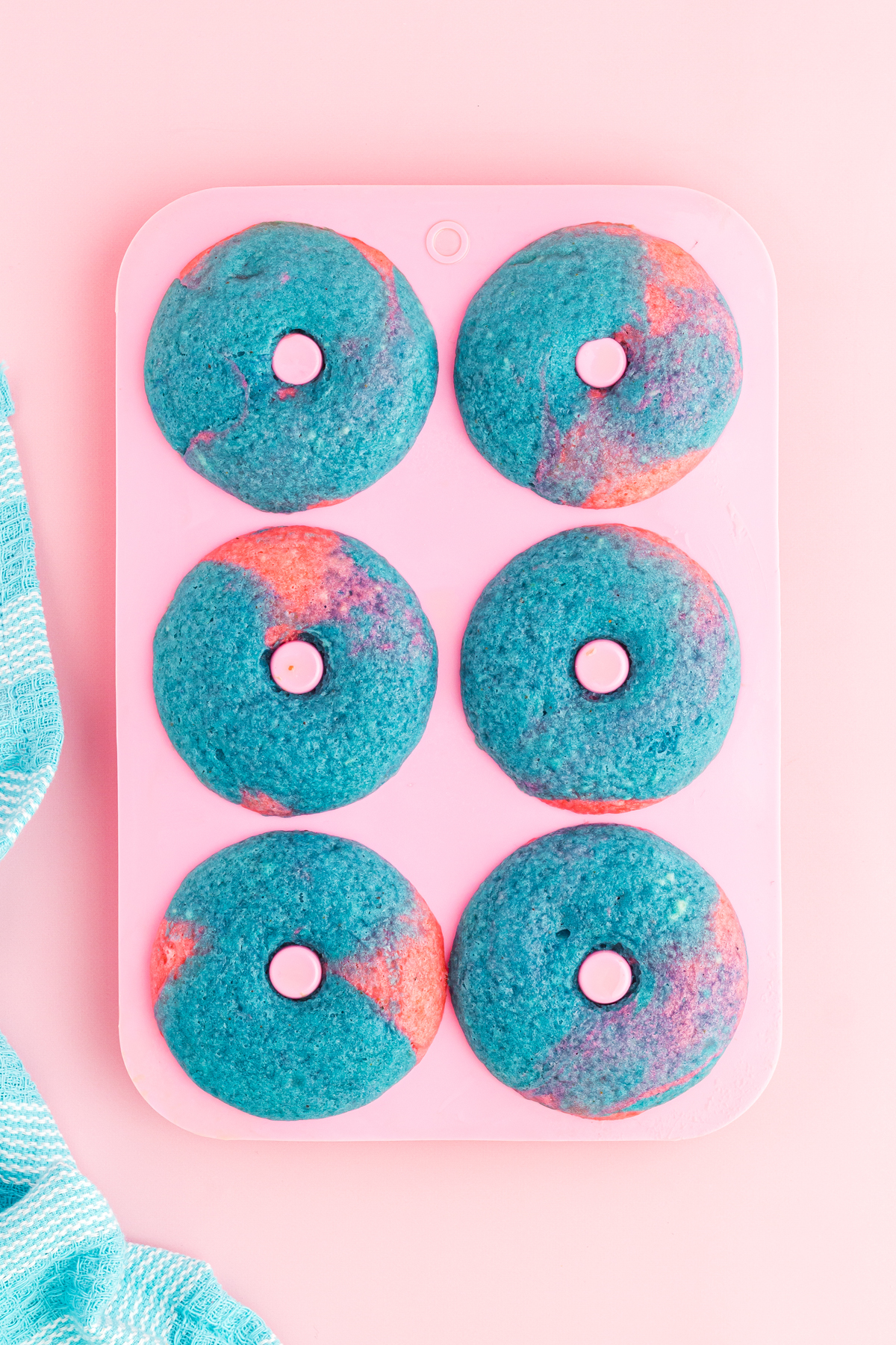 6 blue and pink mixed baked donuts in their pink donut pan on a pink background